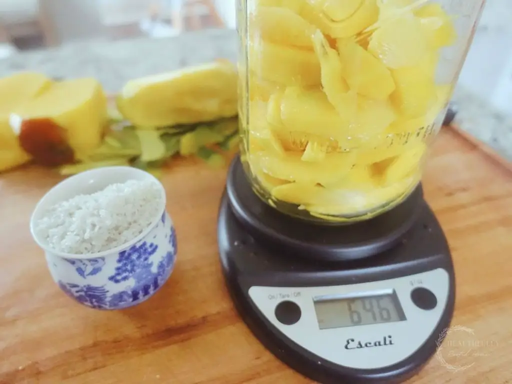 mangos inside a mason jar on top of a kitchen scale with sea salt beside it and mango cores behind