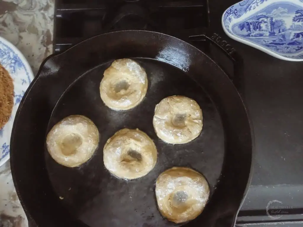 sourdough donuts frying in a cast iron skillet next to blue and white plates