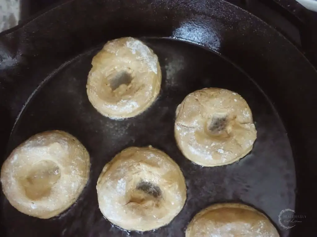 sourdough donuts frying on a cast iron skillet