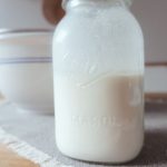 raw kefir in a mason jar on top of a grey placemat in front of a ceramic bowl with blue stripes