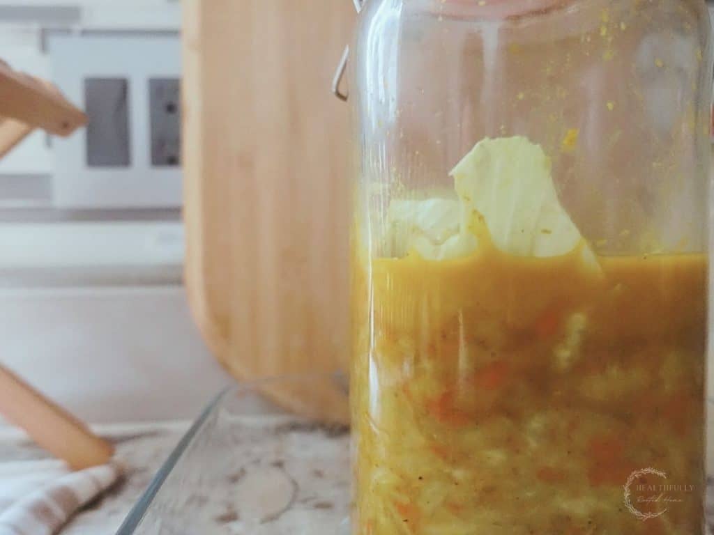 curry kraut in a fermenting jar on a granite countertop with a cutting board in the back