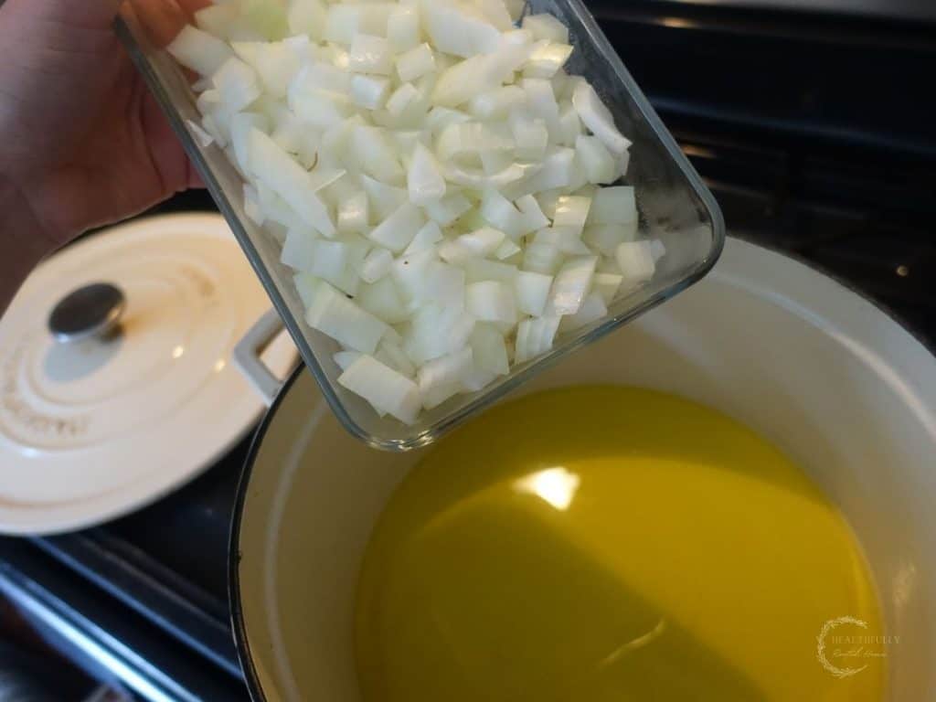 pouring diced onions into a white dutch oven full of olive oil