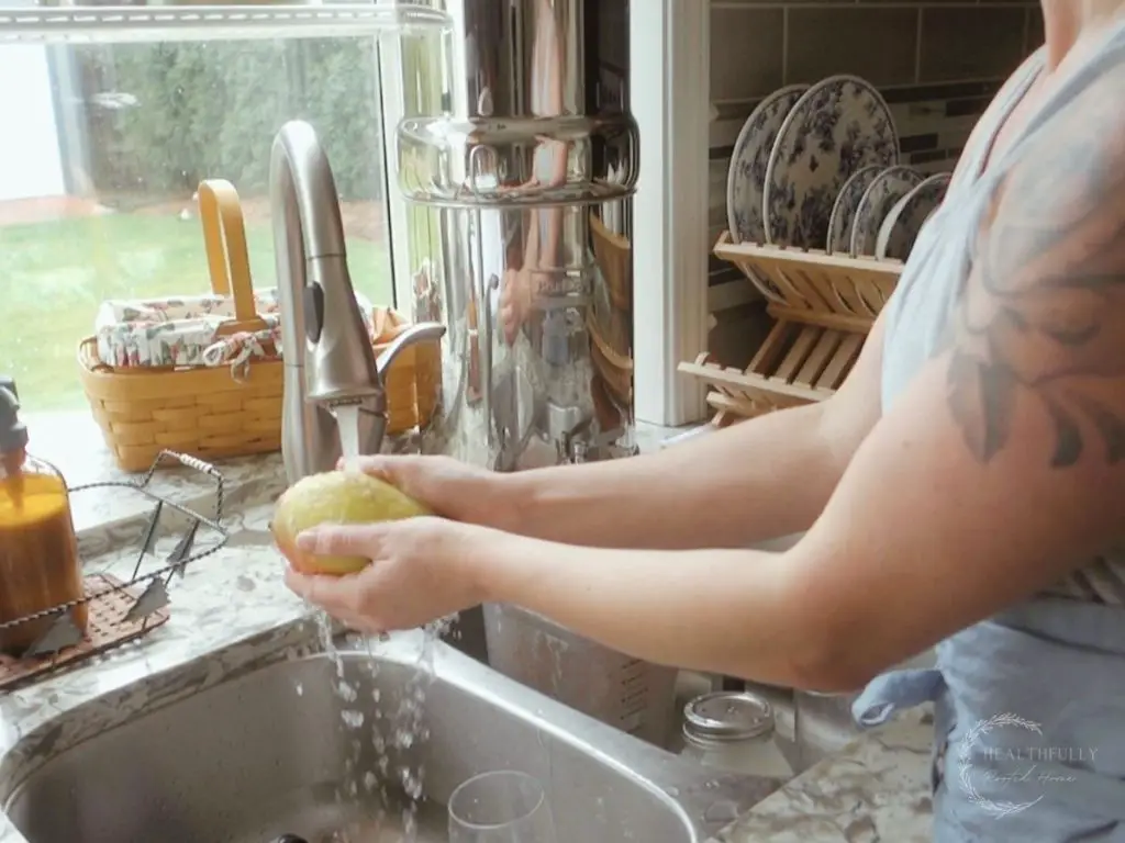 washing a mango in a sink with a berkey water filter and baskets in the background