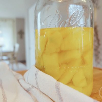 fermented mangos in a large mason jar next to a blue and white striped tea towel with a cross in the background