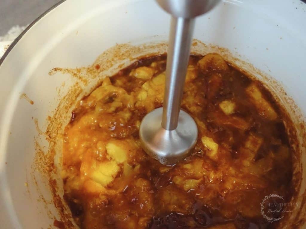 using an immersion blender to blend fermented mango chutney in a white dutch oven