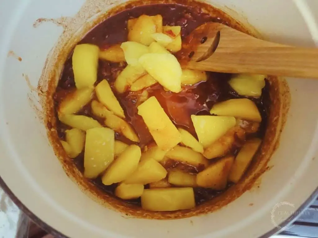 diced fermented mangos inside chutney in a white dutch oven with a smiley face wooden spoon