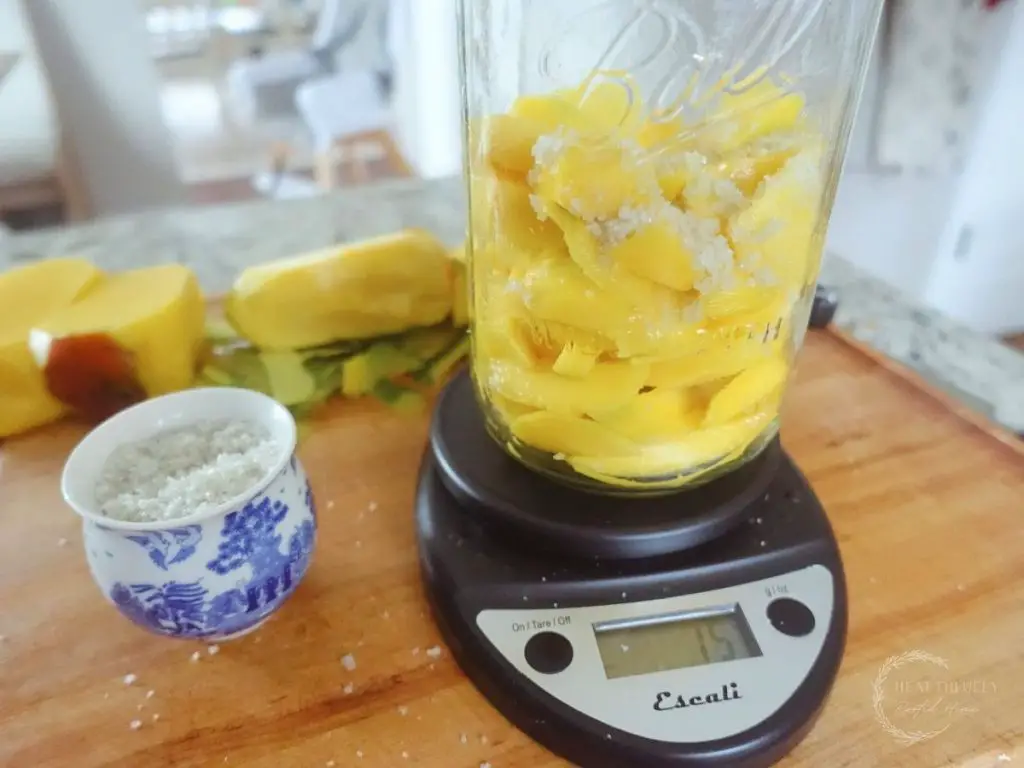 sea salt on top of the diced mangos in a mason jar being weighed on a kitchen scale