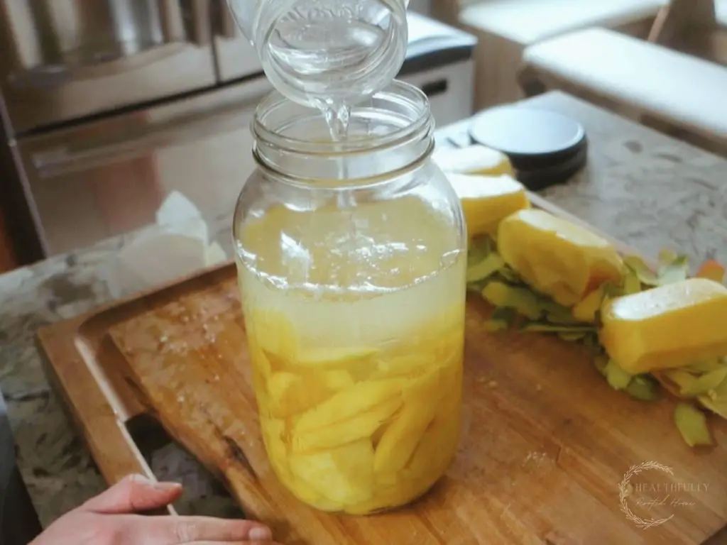 pouring filtered water on top of the salt and mangos in a mason jar getting it ready to be fermented