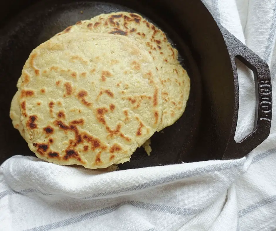 einkorn tortillas using sourdough starter in a lodge cast iron skillet with a blue and white ticking stripe tea towel beside it.