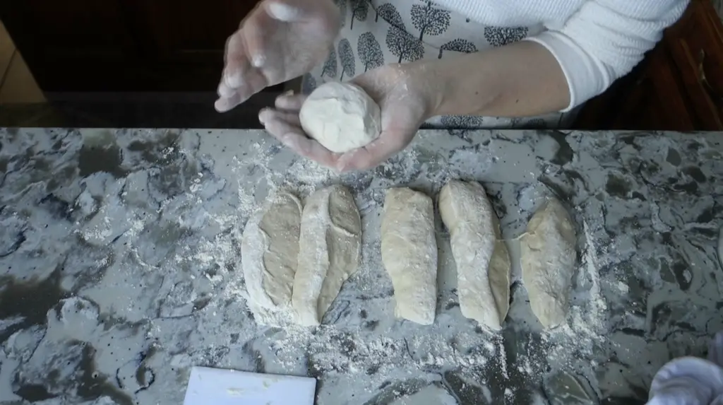 shaping sourdough into a ball of dough with strips of dough below and a dough scraper 