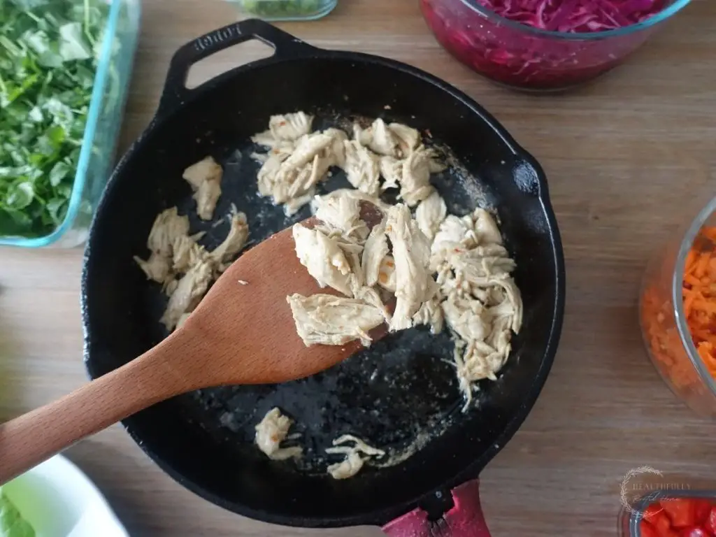 thai coconut lime chicken in a cast iron skillet with a scoop on chicken on a wooden spoon