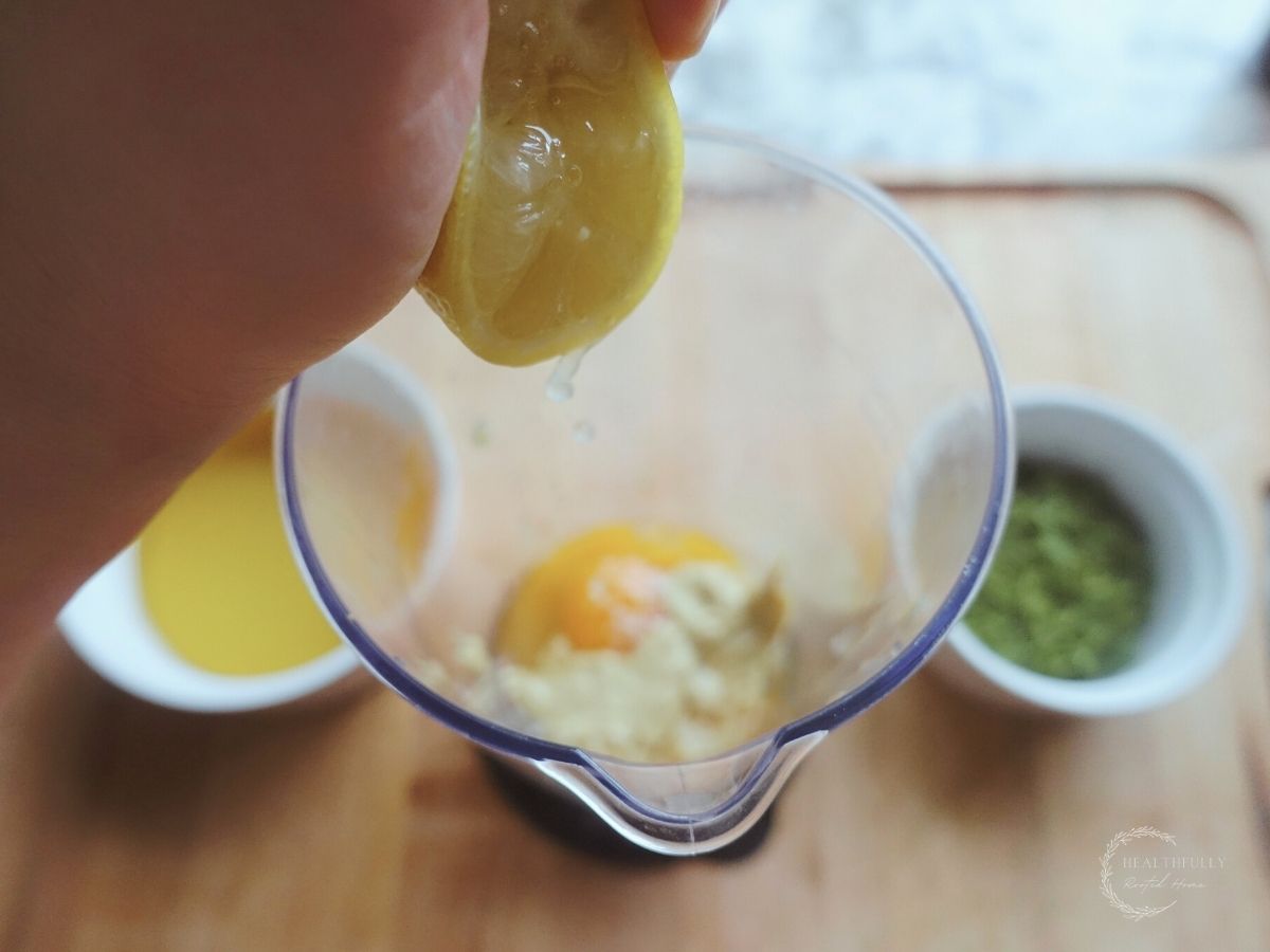squeezing lemon juice from a fresh lemon into the cup of an immersion blender