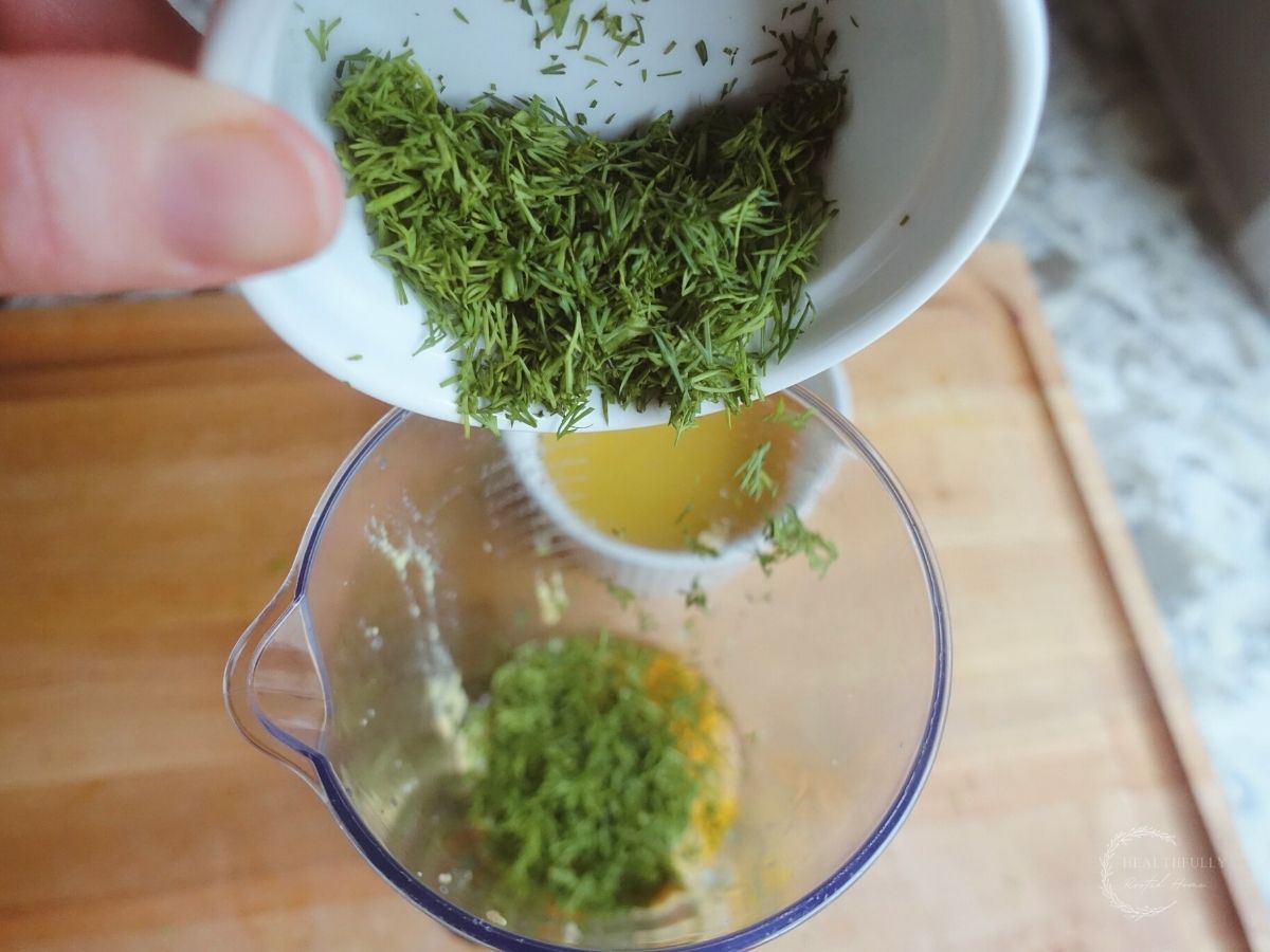pouring fresh dill into cup of immersion blender
