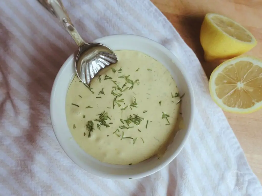 dill aioli with spoon and lemons on the side garnished with fresh dill