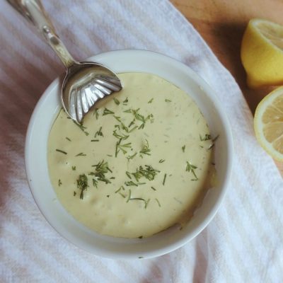 dill aioli with spoon and lemons on the side garnished with fresh dill