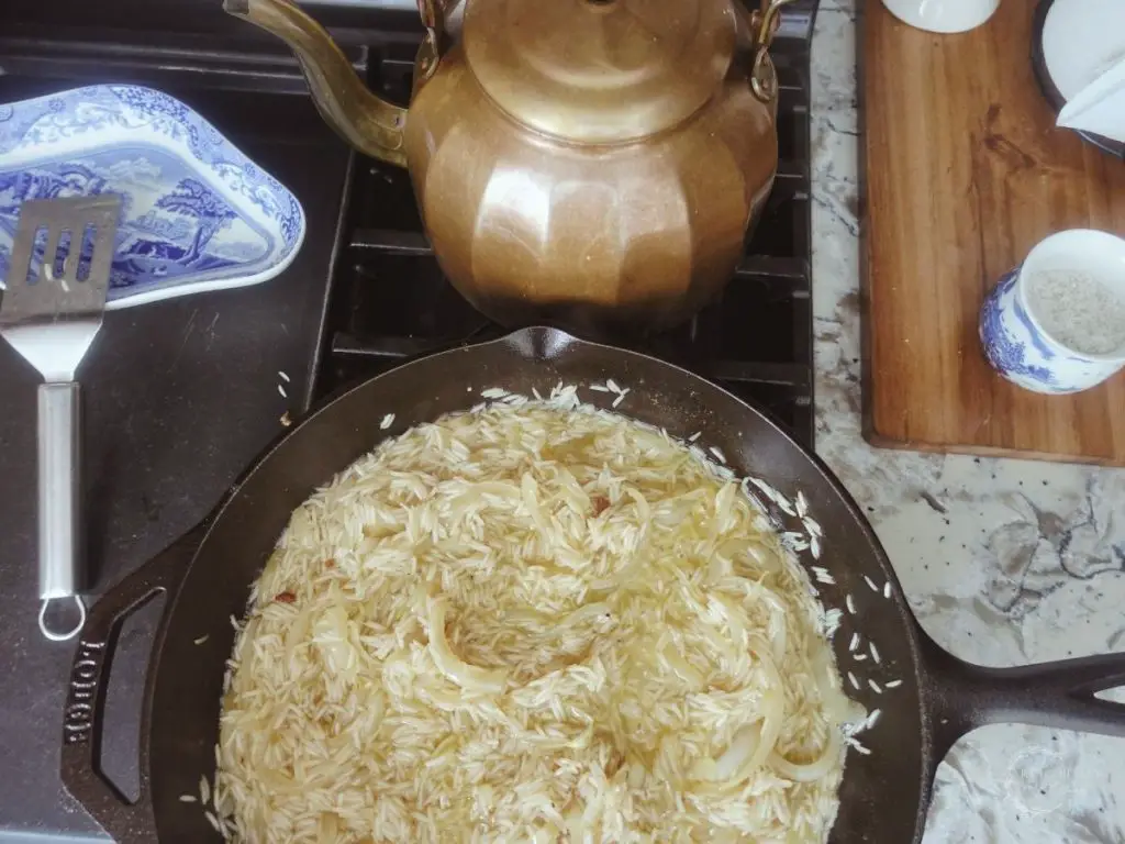 saucy risotto basmati in a cast iron skillet with a spatula on a blue and white china plate and a copper tea kettle in the back