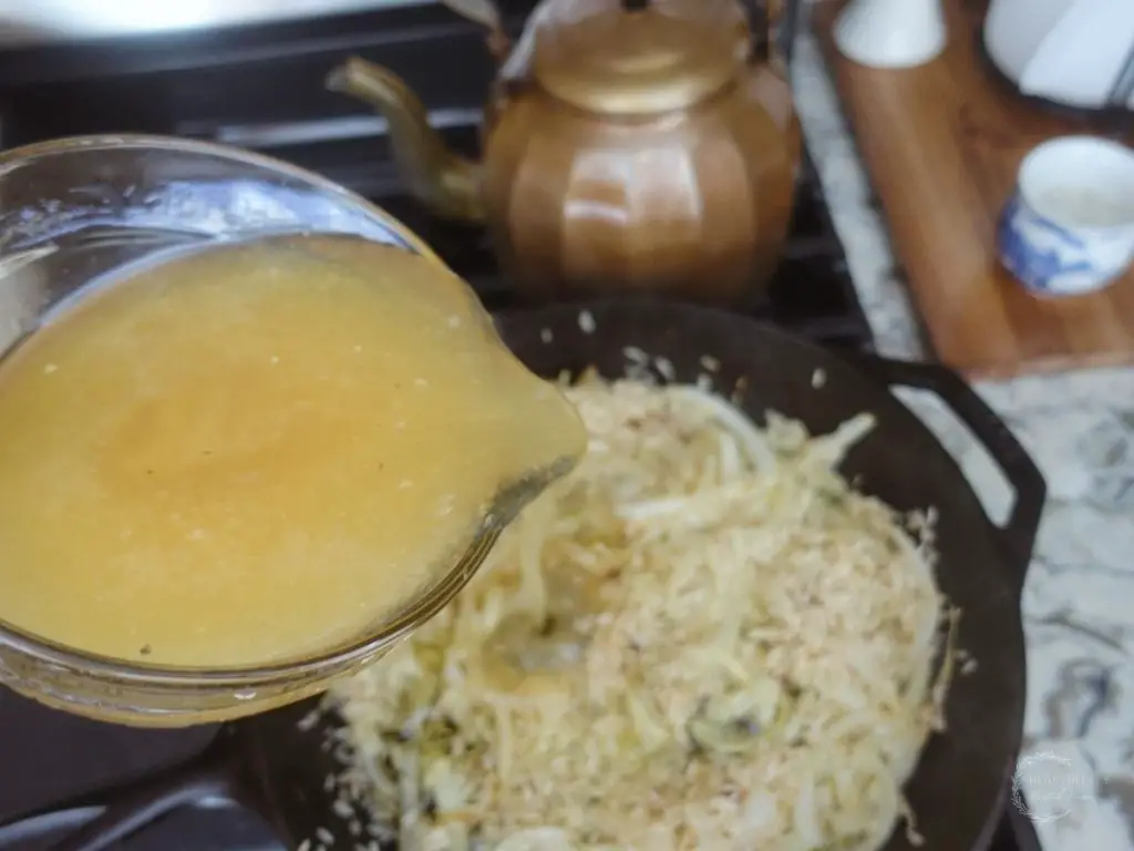 pouring bone broth into the cast iron skillet with onions and basmati rice 