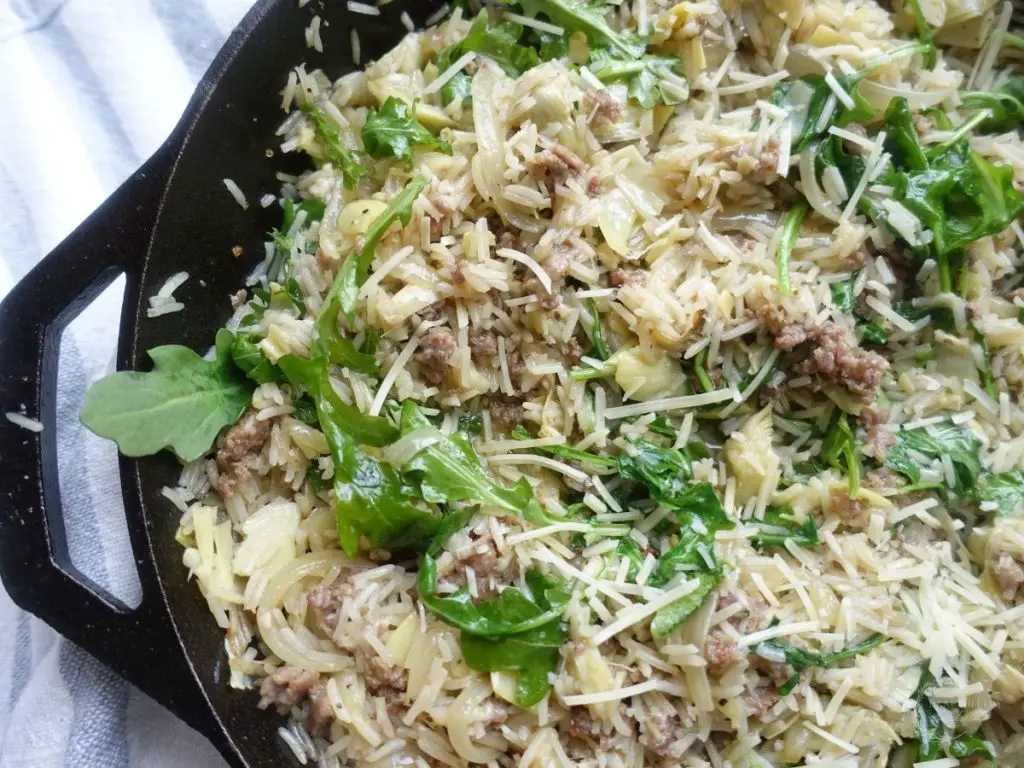 risotto dish made with basmati rice with arugula sausage and artichokes inside a cast iron skillet