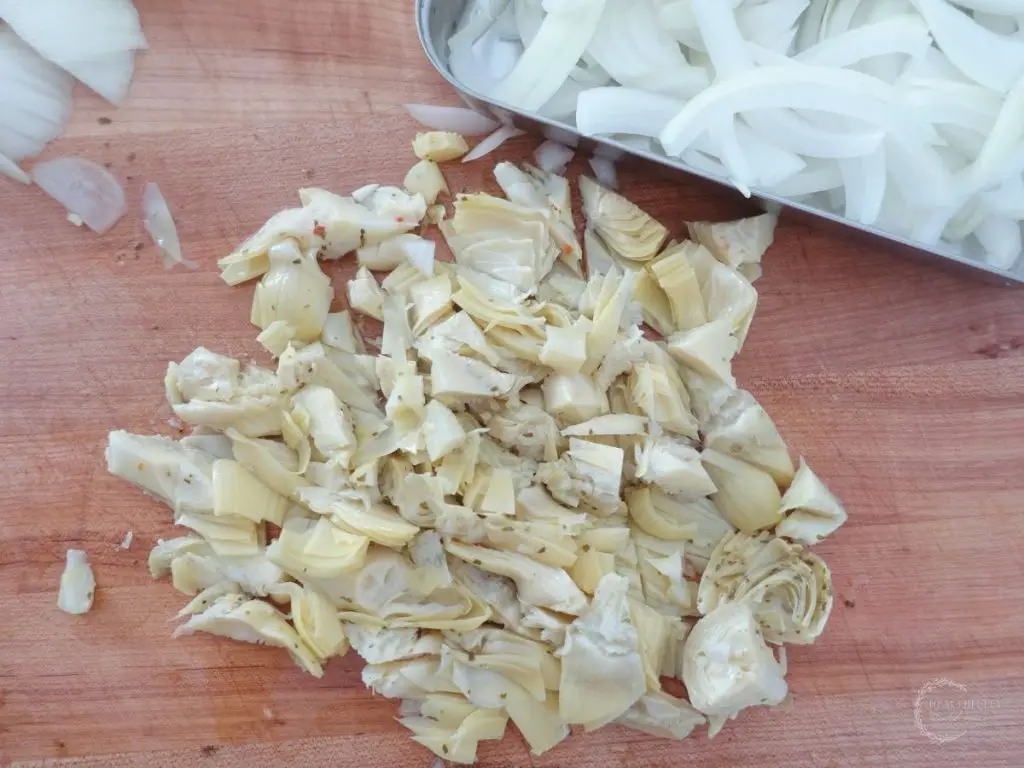 diced artichoke hearts and sliced yellow onion on a wooden boos block cutting board
