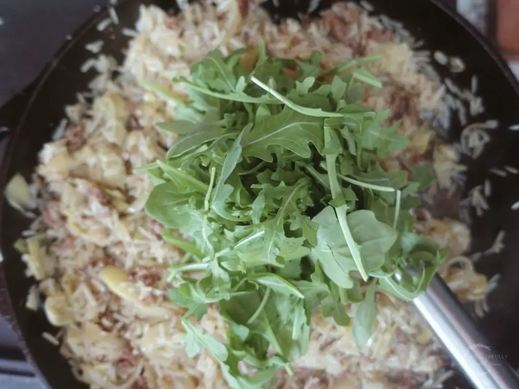 arugula on top of risotto in a cast iron skillet with a spatula hanging out