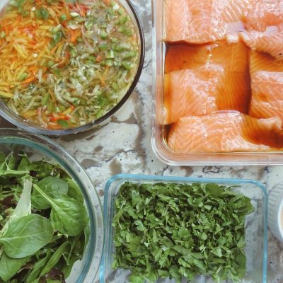 ingredients for salmon banh mi salad in clear glass containers on marble countertop with raw salmon pickled veggies spring greens cilantro and ancho aioli