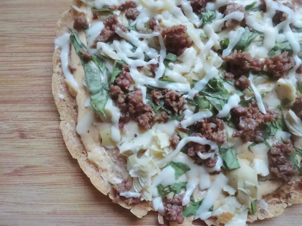 same day sourdough pizza crust with italian sausage arugula white sauce and cheese on top of a wooden cutting board