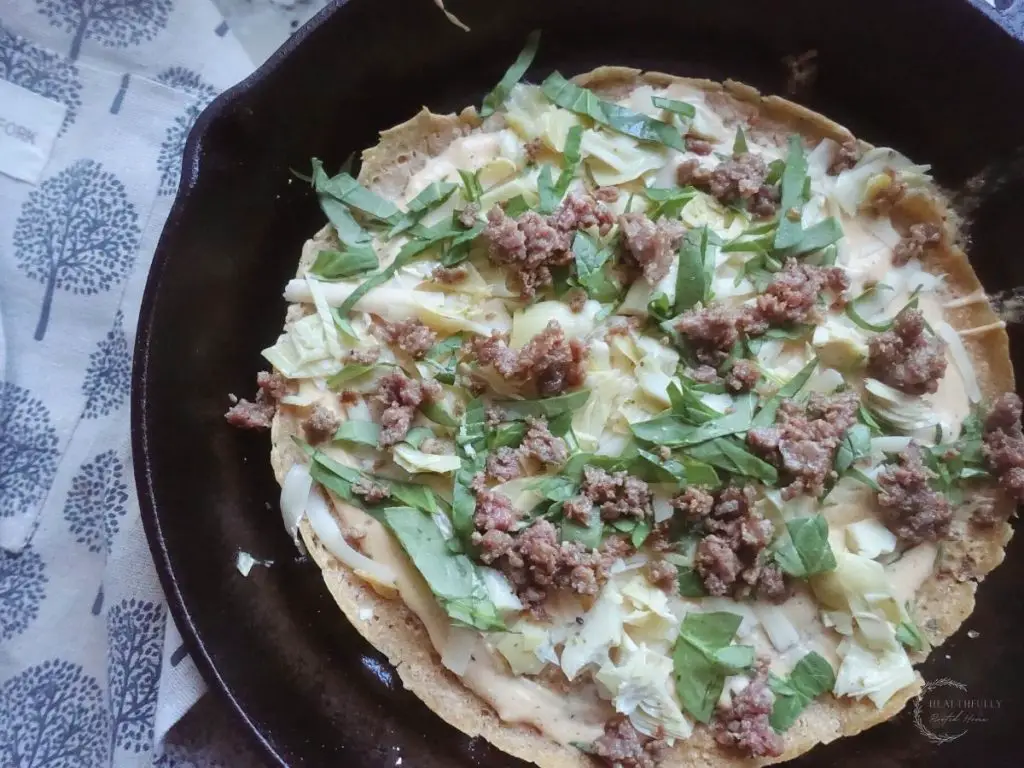 sourdough pizza in a cast iron skillet with arugula italian sausage and white sauce