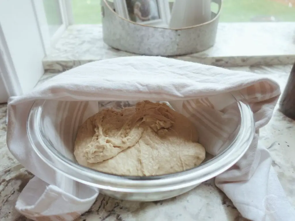 sourdough proofing in a glass bowl with a white tea towel overtop