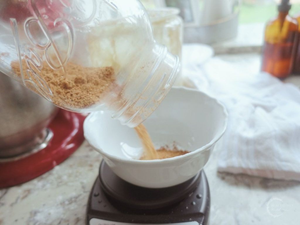 pouring brown sugar into a bowl with a scale out of a mason jar to measure the grams