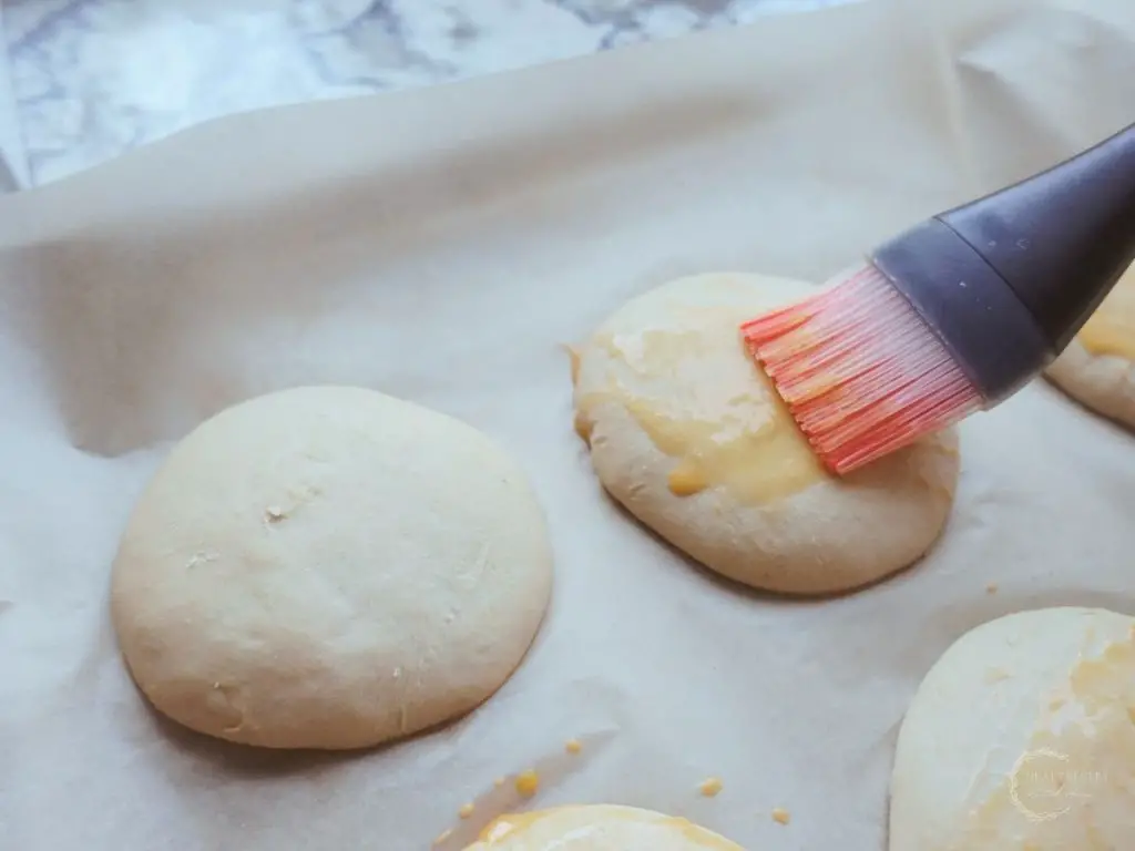 brushing the bun dough with a pastry brush with red bristles spreading egg wash on top of the buns