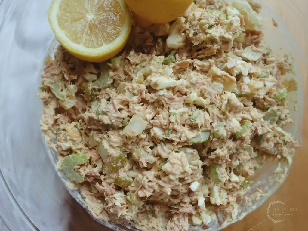 southern tuna salad recipe in a glass bowl with a white tea towel on the side and halved lemons as garnish