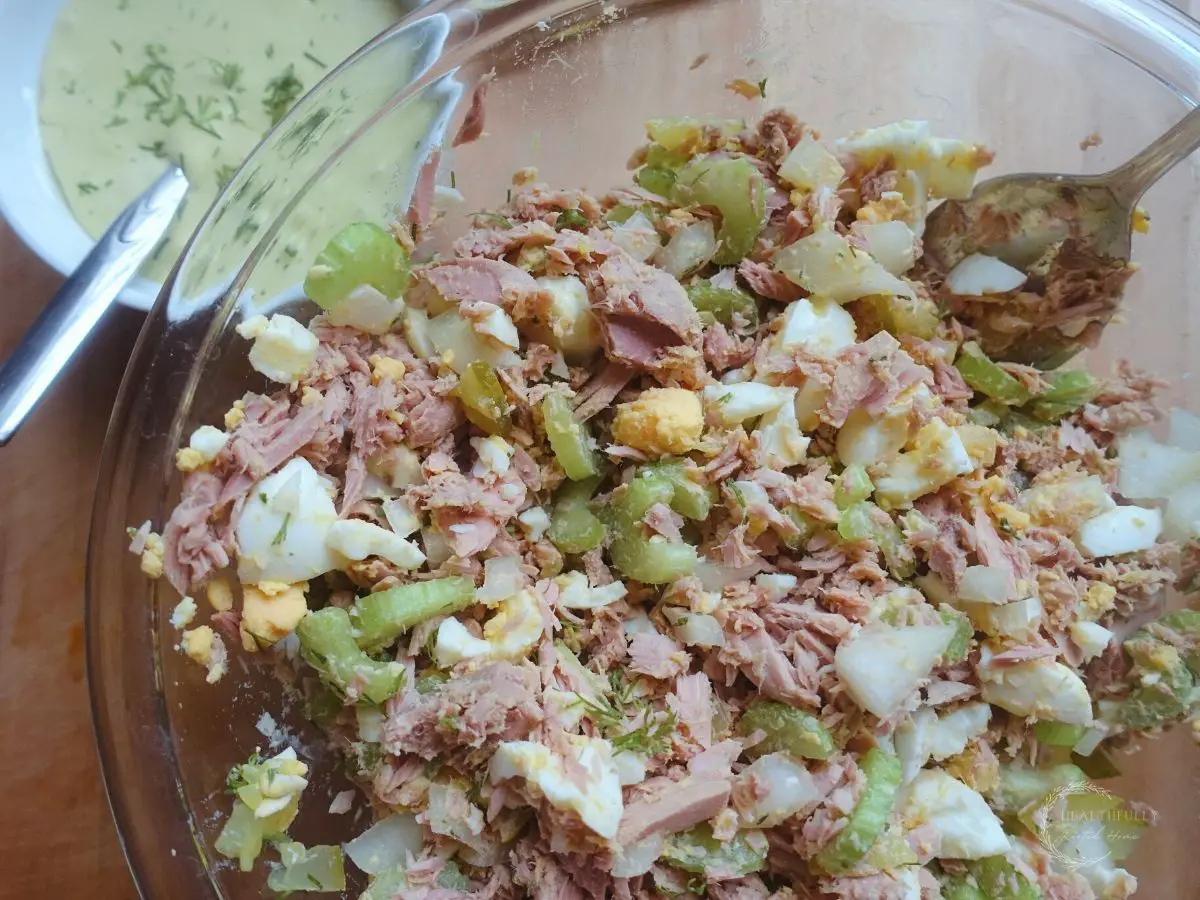 tuna salad dry ingredients tossed into a large glass bowl with dill aioli on the side
