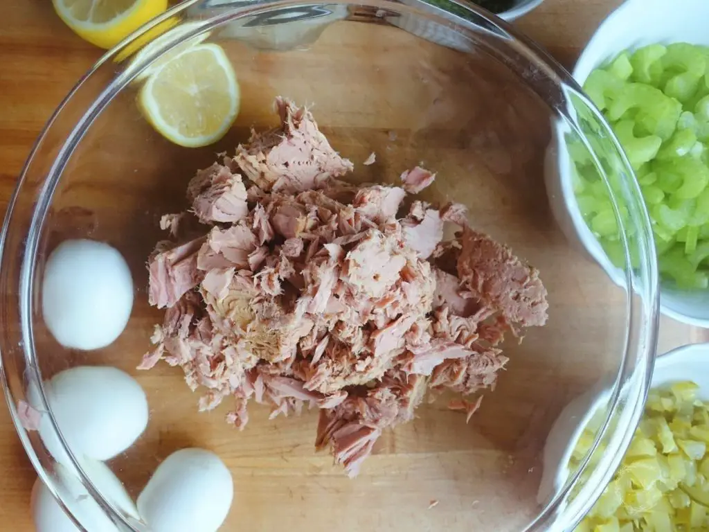 ingredients for tuna salad with tuna in the center in a clear glass bowl and the other ingredients surrounding it