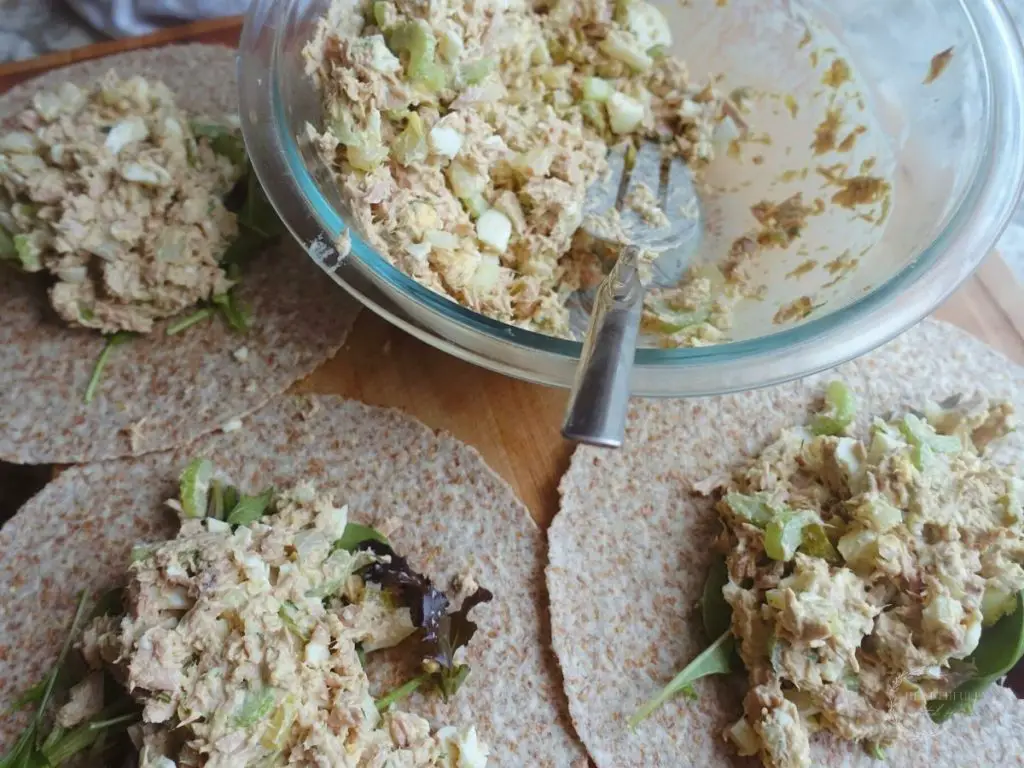 tuna salad on top of greens inside of 3 tortillas with a bowl of tuna salad next to them