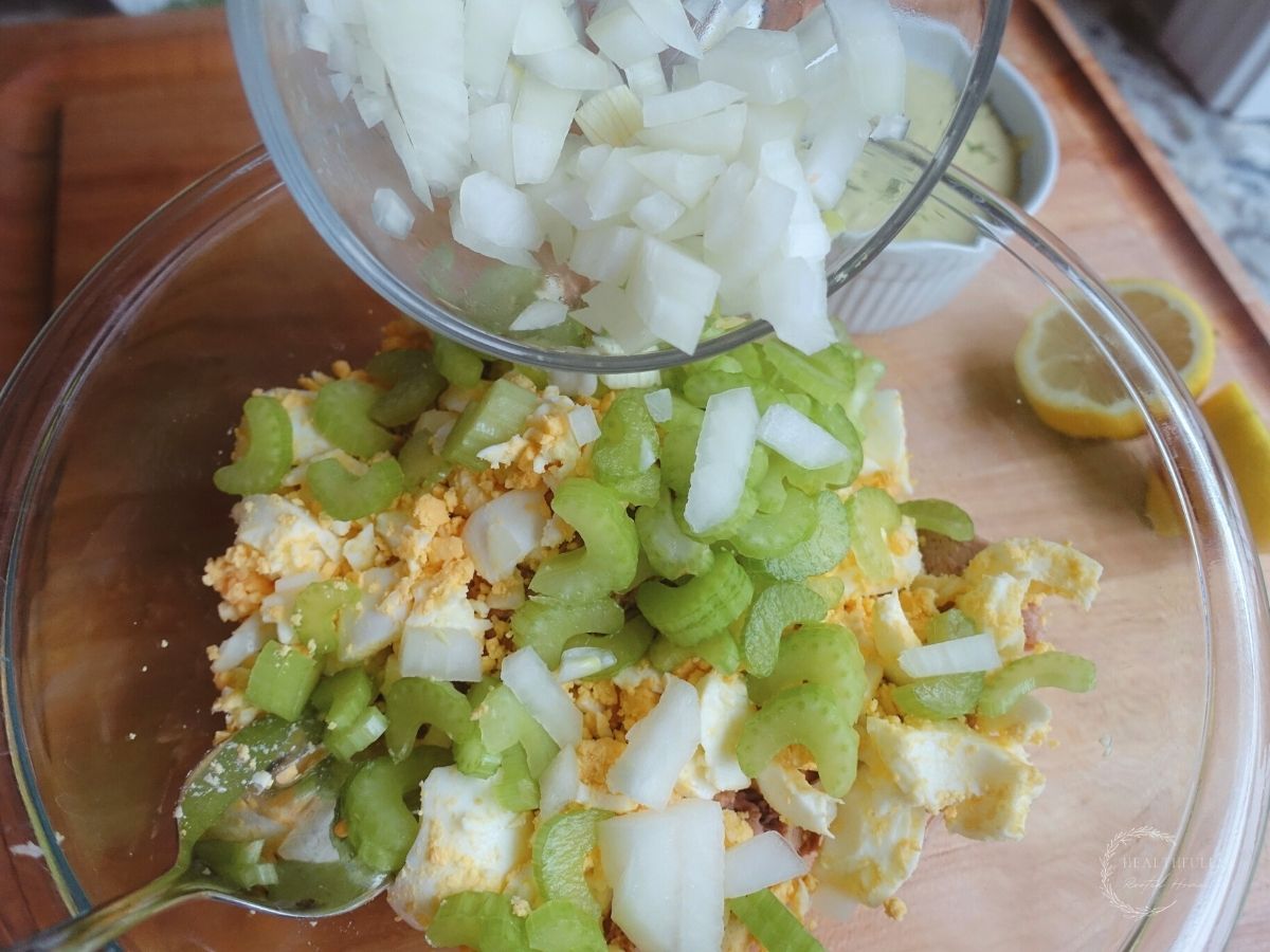 pouring white onions into a bowl with tuna eggs and celery