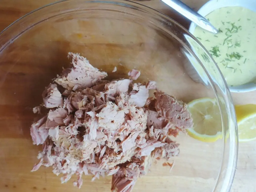 canned tuna in a large glass bowl with dill aioli and lemons to the side