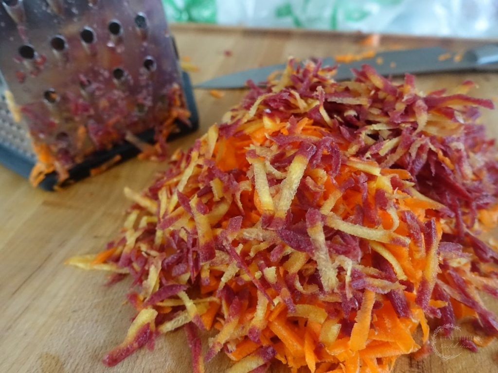 shredded carrots with a grater in the background on a wooden cutting board. 