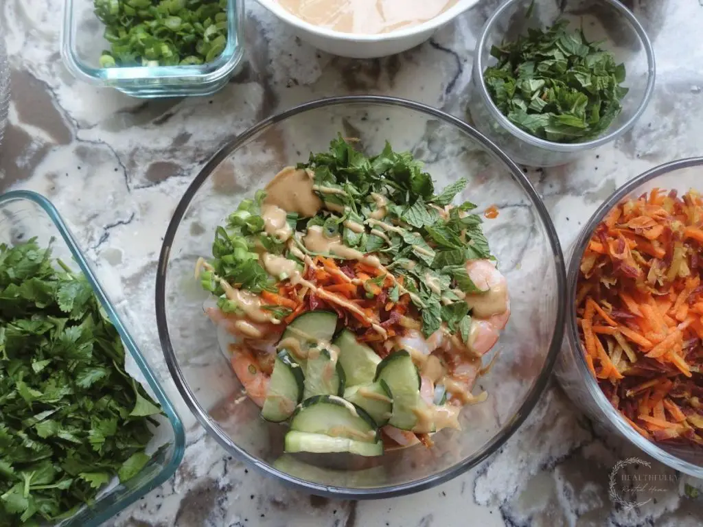 spring roll in a bowl with veggies and shrimp and peanut sauce surrounding it