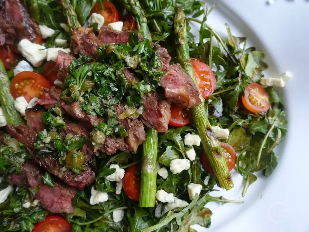 steak arugula salad with salsa gremolata on top the steak and grilled asparagus with cherry tomatoes and smaked blue cheese