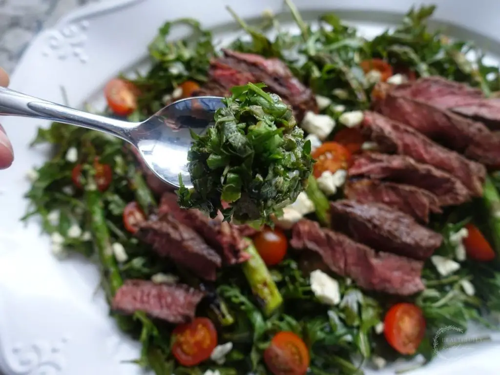 salsa gremolata drizzled on steak arugula salad on a white plate