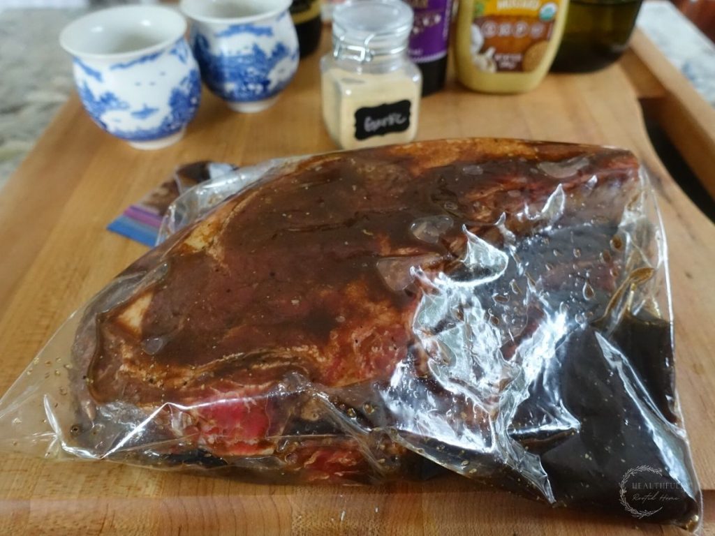 steak marinading in a plastic bag with spices in the background on a wooden cutting board