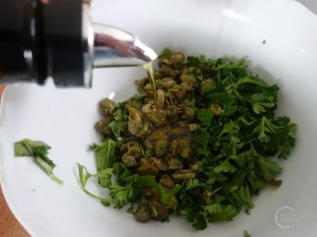 drizzling olive oil overtop the salsa gremolata inside of a white bowl