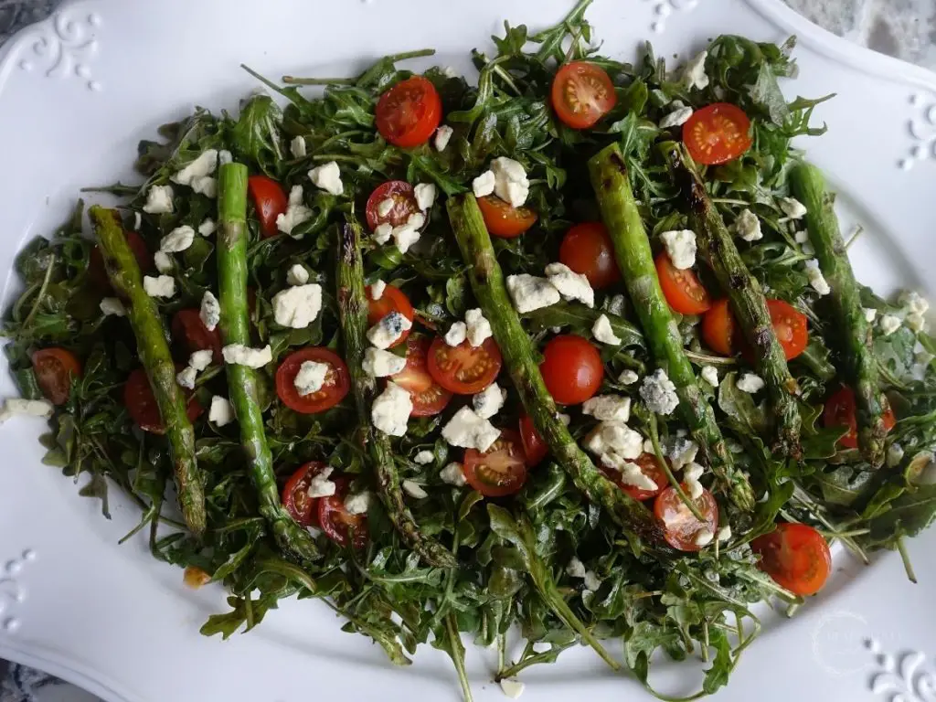 arugula salad with grilled asparagus smoked blue cheese and cherry tomatoes on a white platter