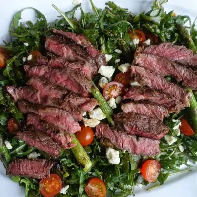 steak and arugula salad with grilled ribeye, grilled asparagus, balsamic dressed arugula cherry tomatoes and smoked blue cheese on a white platter