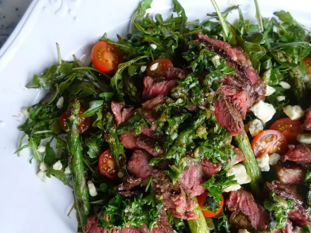steak salad on a white platter with smoked blue cheese arugula and grilled asparagus 