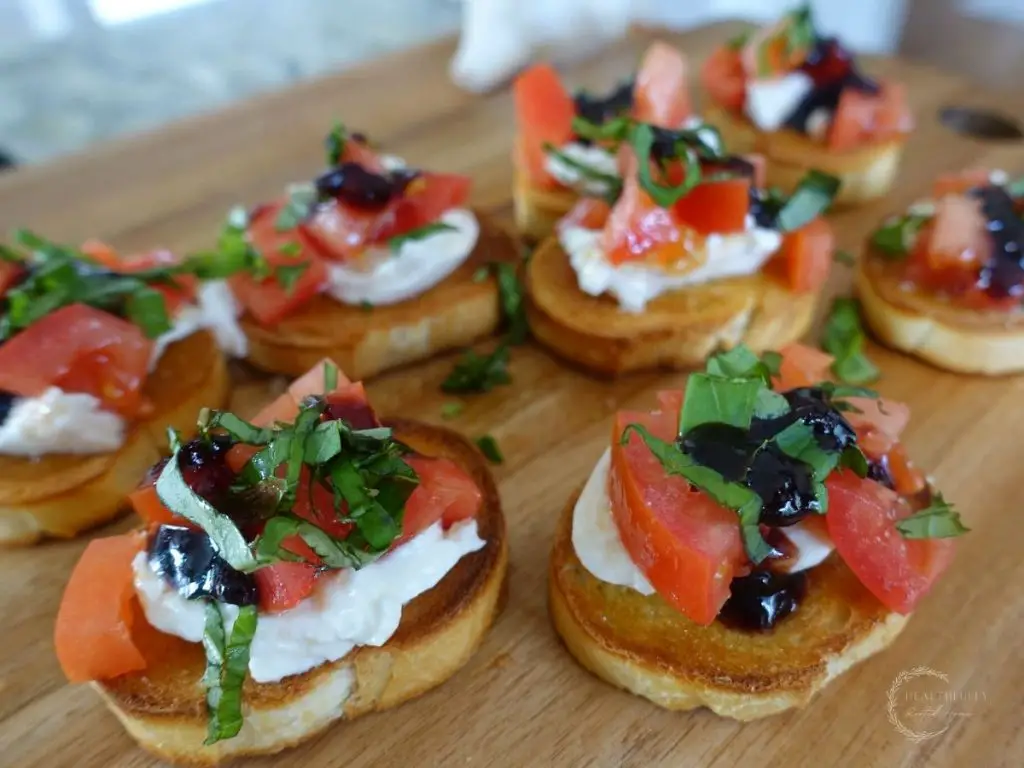crostini topped with burrata and a tomato and olive oil mixture drizzled with balsamic fig glaze and topped with basil