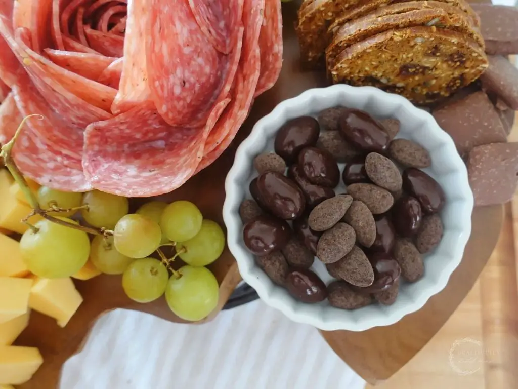 side of a salami rose on a charcuterie board with chcocolate covered almonds and grapes