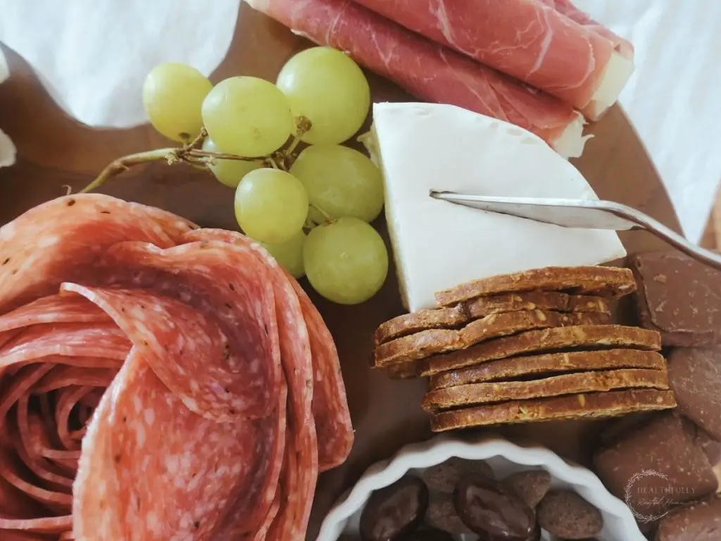 small charcuterie board with a quarter of a brie cheese wheel with a cheese knife sticking out grapes on the side crackers leaning against it
