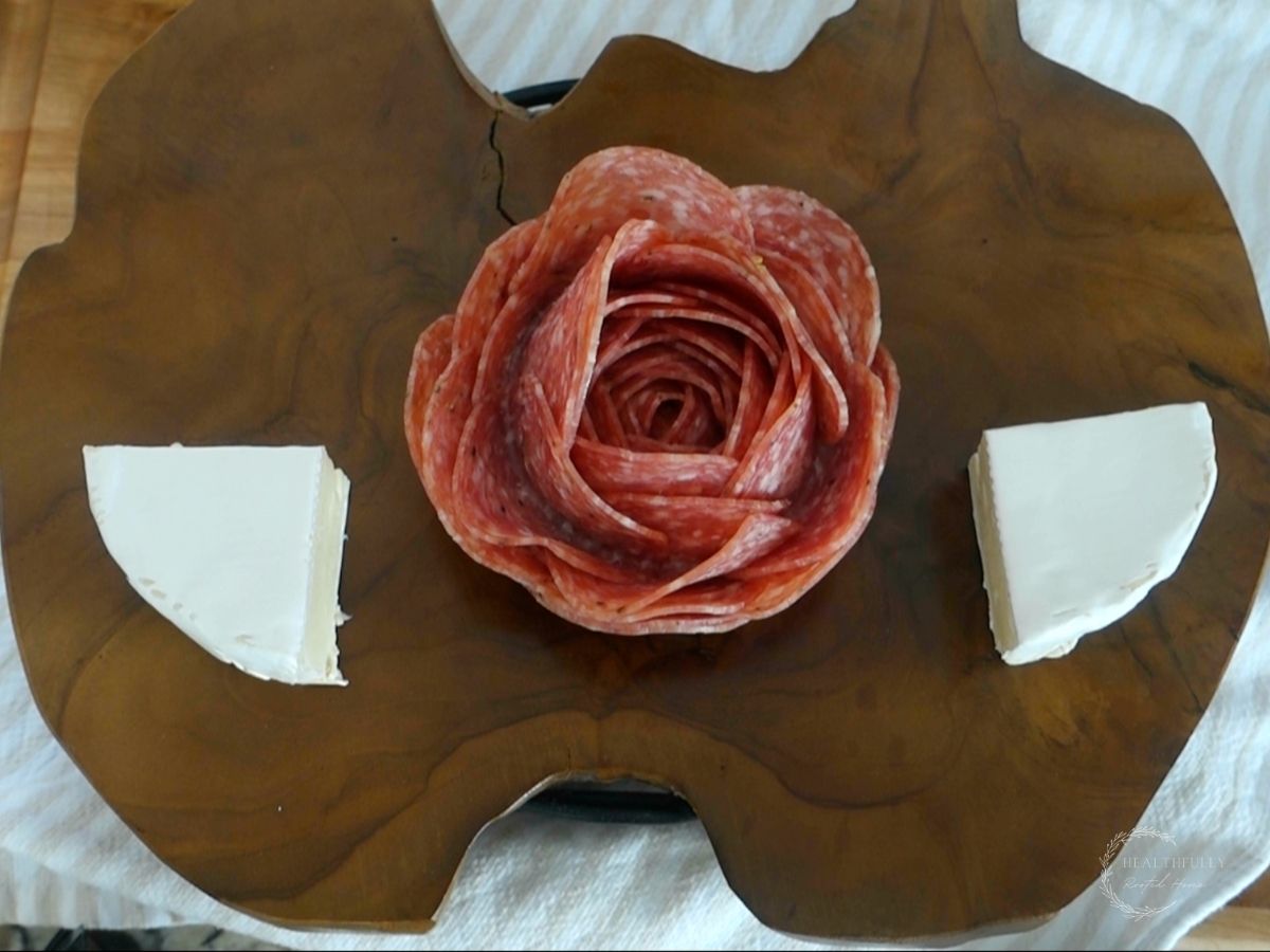 salami rose with brie cheese on either side with a wooden charcuterie platter