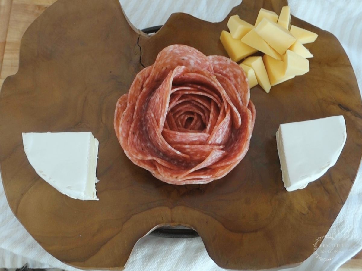 salami rose on a wooden charcuterie platter with brie cheese and smoked gouda triangles